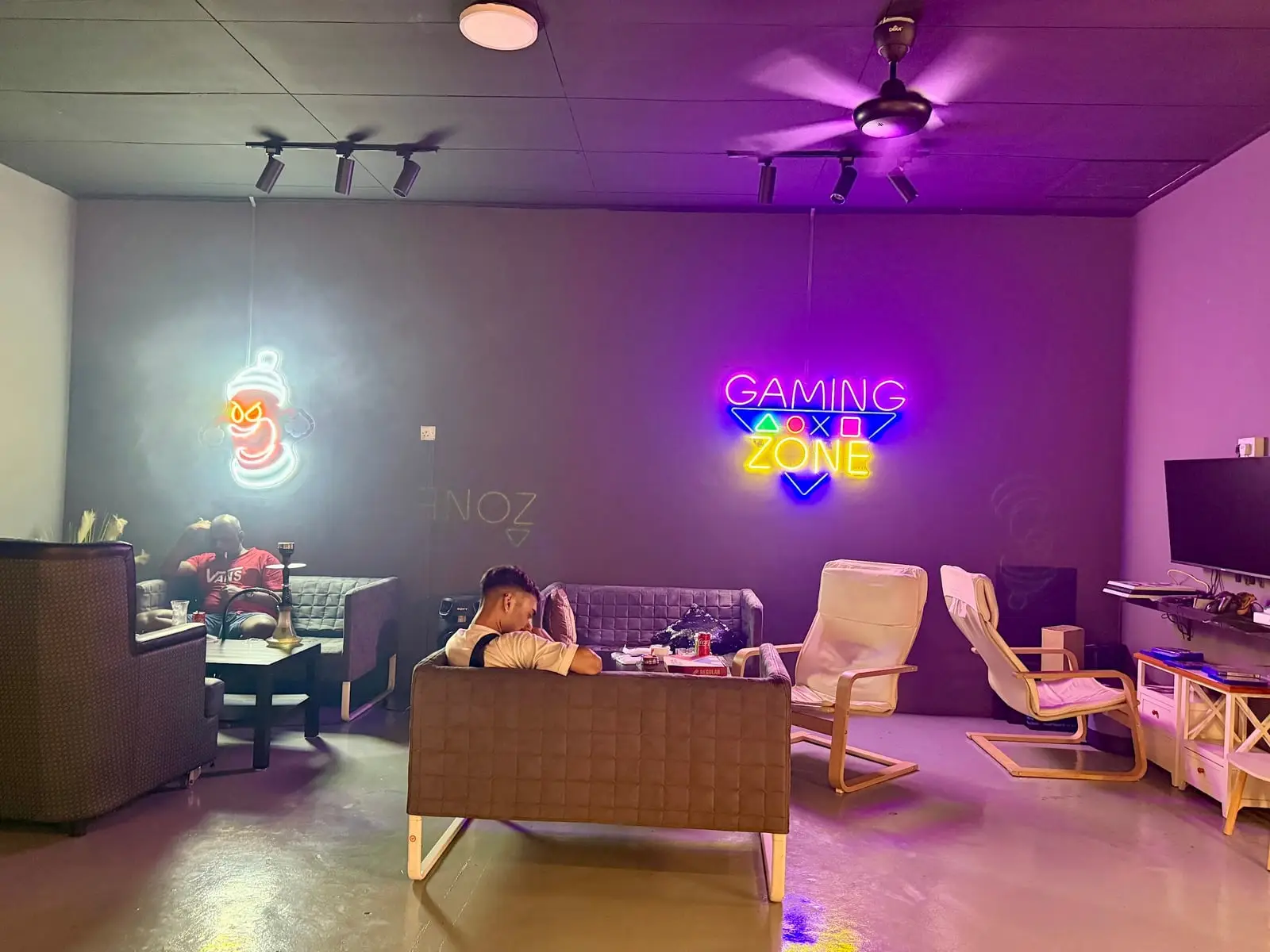 The lounge at night: sofas and armchairs in purple light, with neon signs on the far wall.