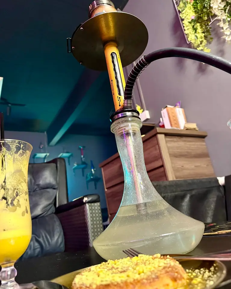 A shisha on a table in the lounge, with a cold drink and a plate of knafeh.