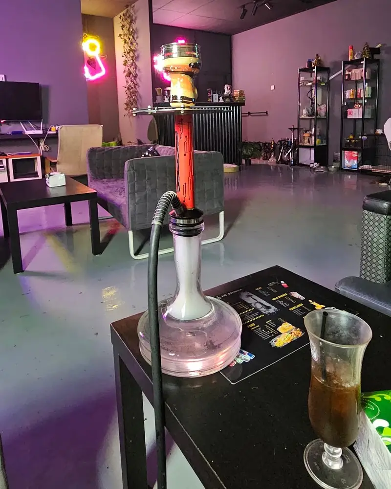 A shisha and a cold drink on a low table, with the lounge's neon lights behind.